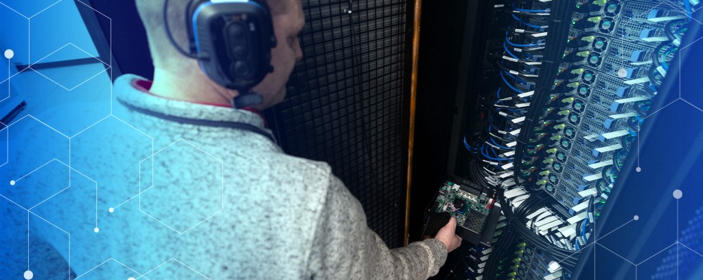 man with headphones on standing next to computer terminal