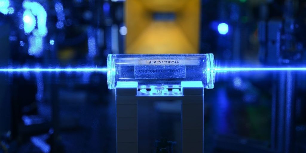 Atoms in a glass vapor cell are excited with laser beams to Rydberg states. They detect the electric fields (coming from the gold antenna in the background) and imprint the information back onto the laser beams (U.S. Army photo).